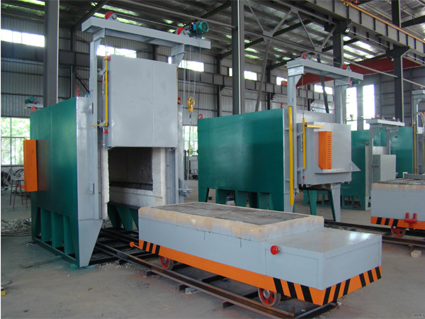 Industrial car-bottom furnace with raised front door and refractory-lined loading car on rails